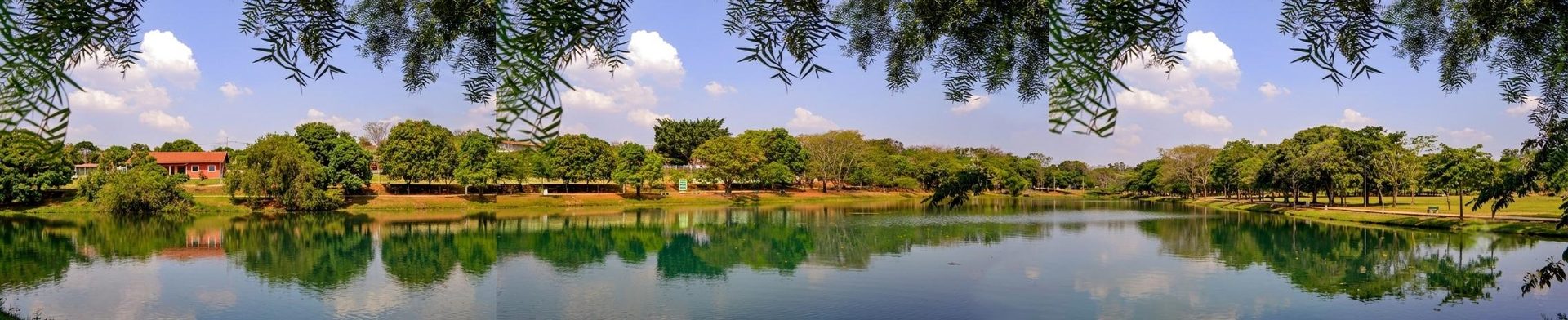 Vista panorâmica do Parque Irmã Dorothy Stang em Hortolândia, com lago cercado por árvores, reflexo do céu na água e casario ao fundo.
